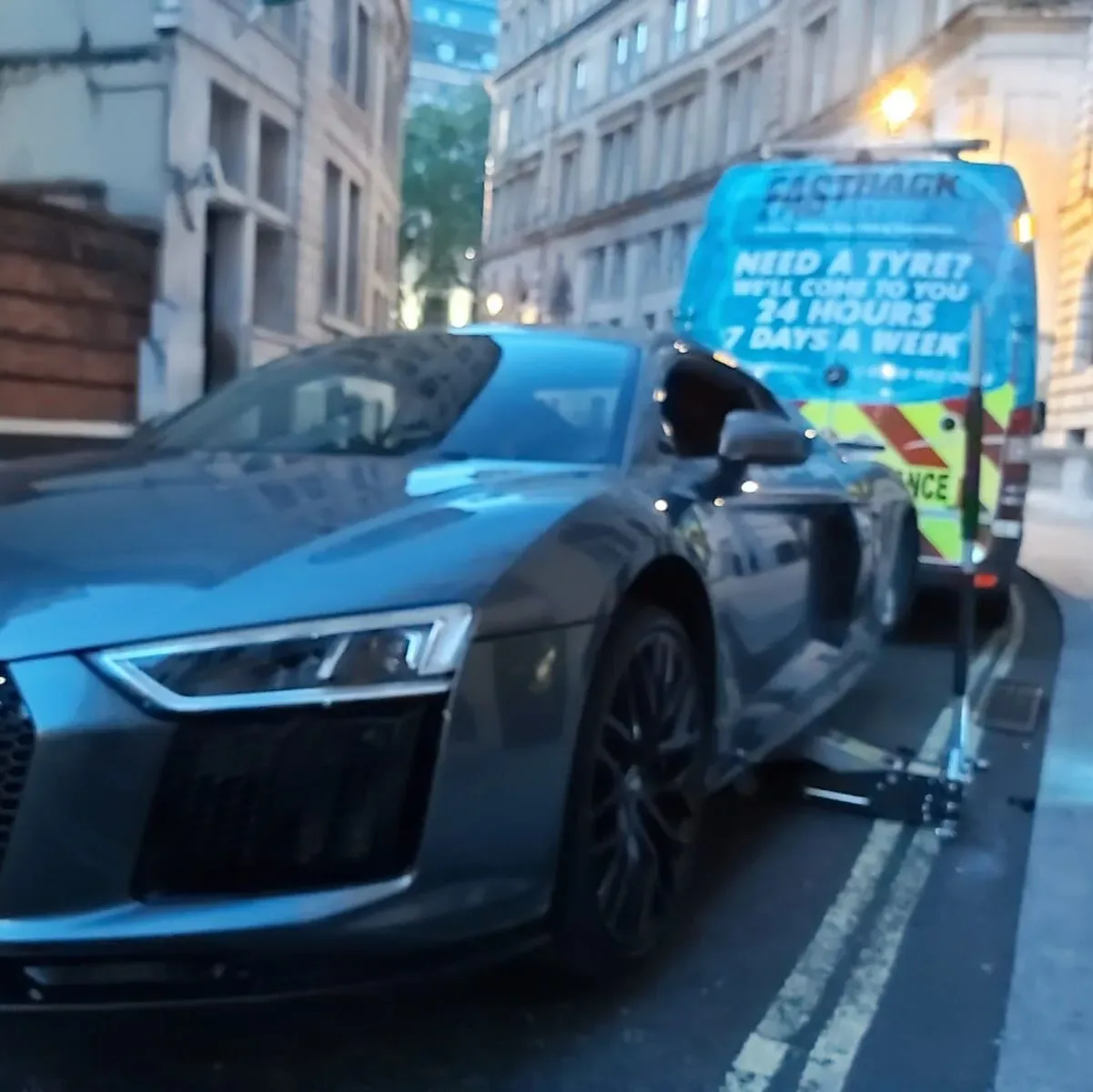 Grey Audi R8 V10 having a wheel changed on a London street at dusk with the Fastrack Tyres van behind