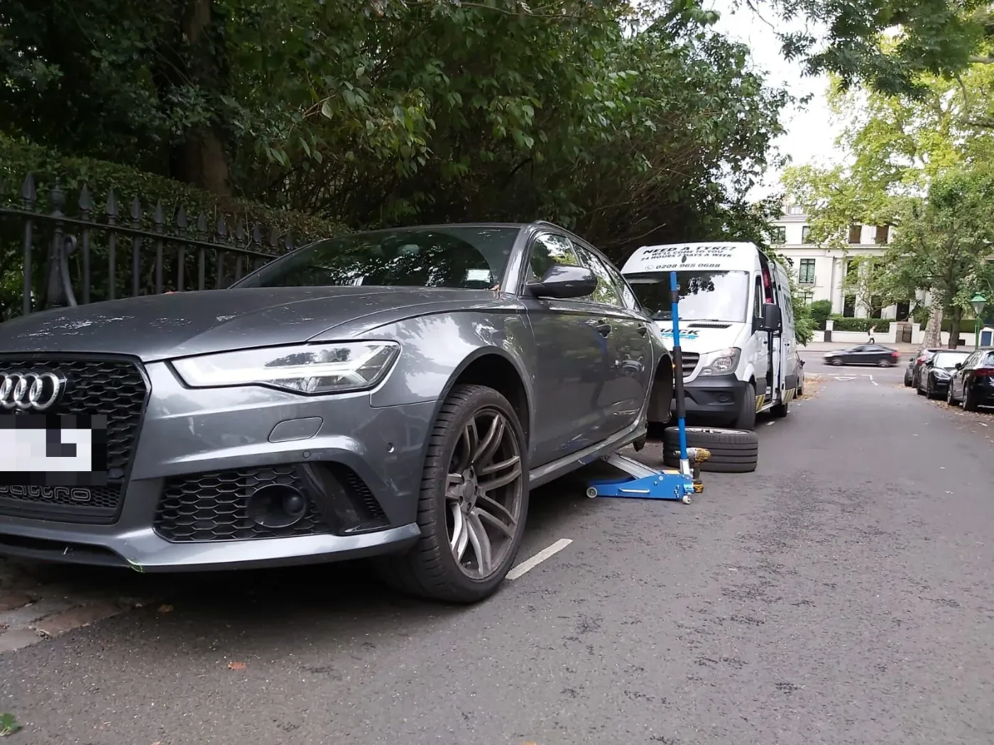 Grey Audi RS6 Avant raised on a trolley jack for a wheel change beside the Fastrack Tyres van in Belgravia