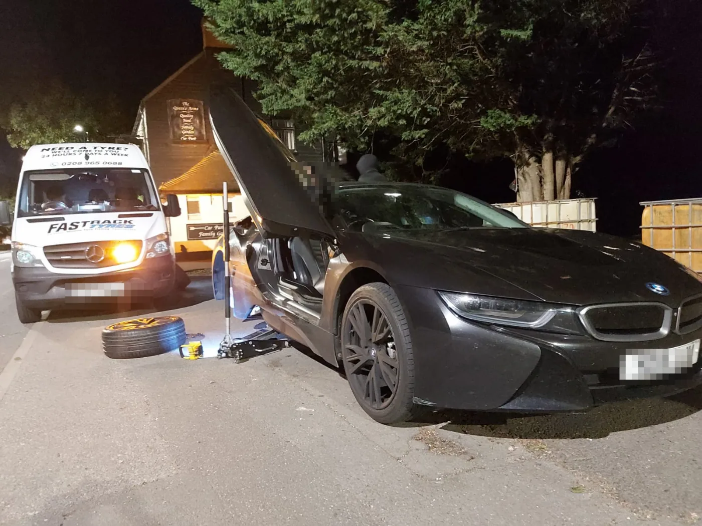 Black BMW i8 hybrid sports car with a wheel removed at a night-time mobile tyre call-out, Fastrack van lighting the scene