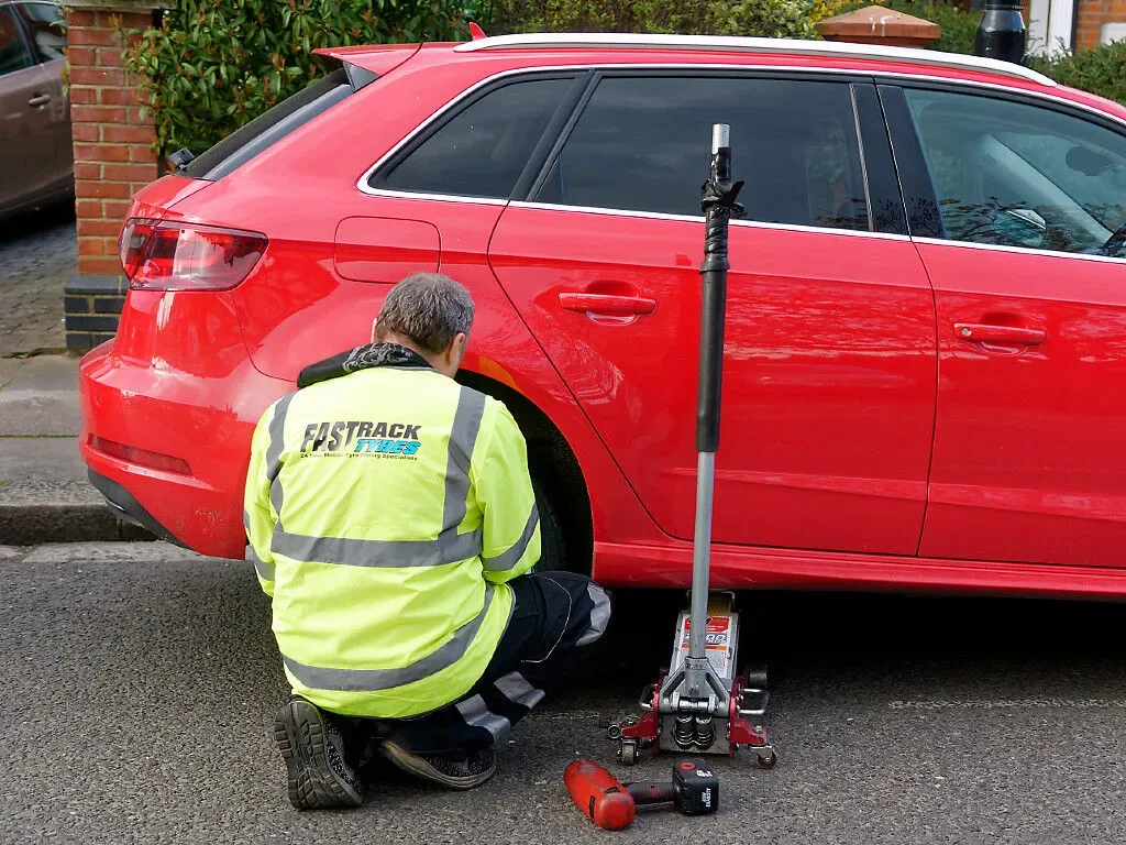 Fastrack Tyres technician in branded hi-vis using a trolley jack and impact wrench on a red Audi A3 at the roadside