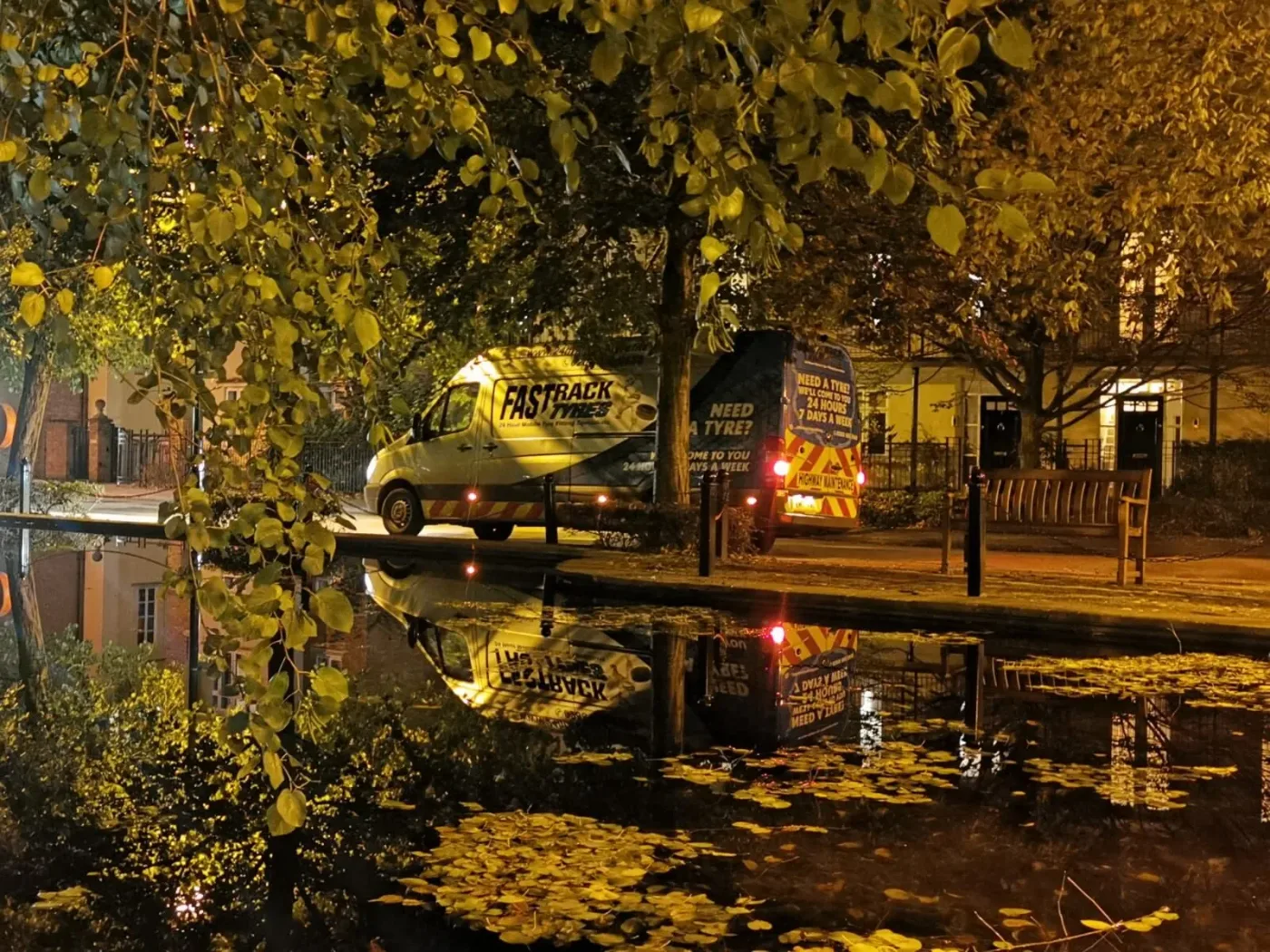 Fastrack Tyres van reflected in a rain-soaked street among autumn leaves at night