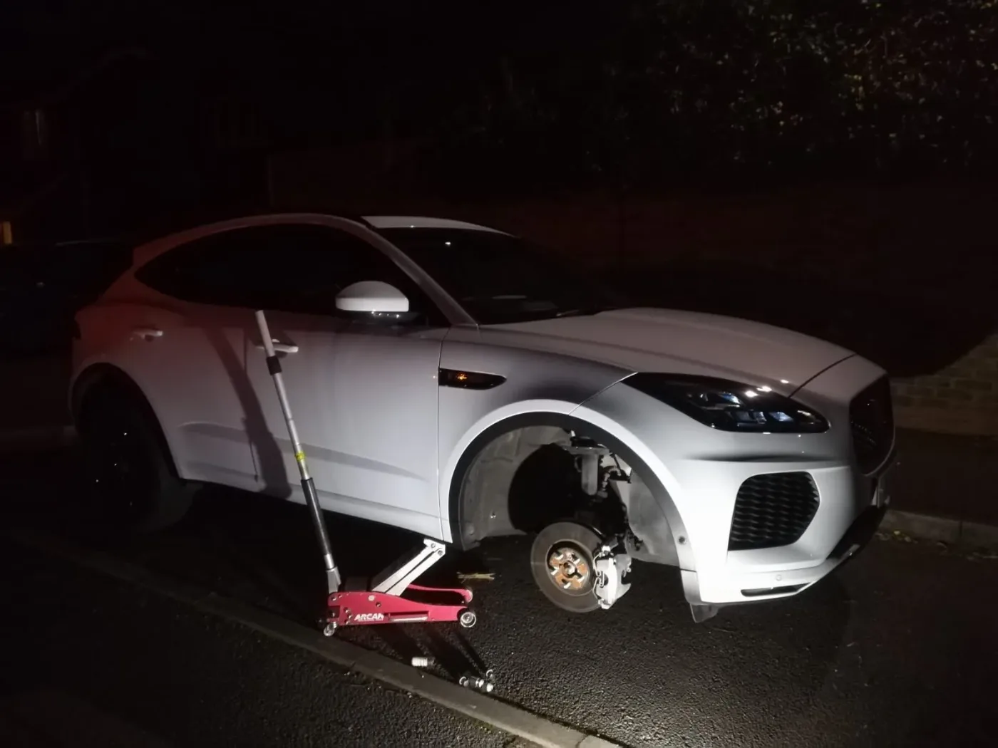 White Jaguar E-Pace jacked up at night with the front wheel removed showing the brake disc