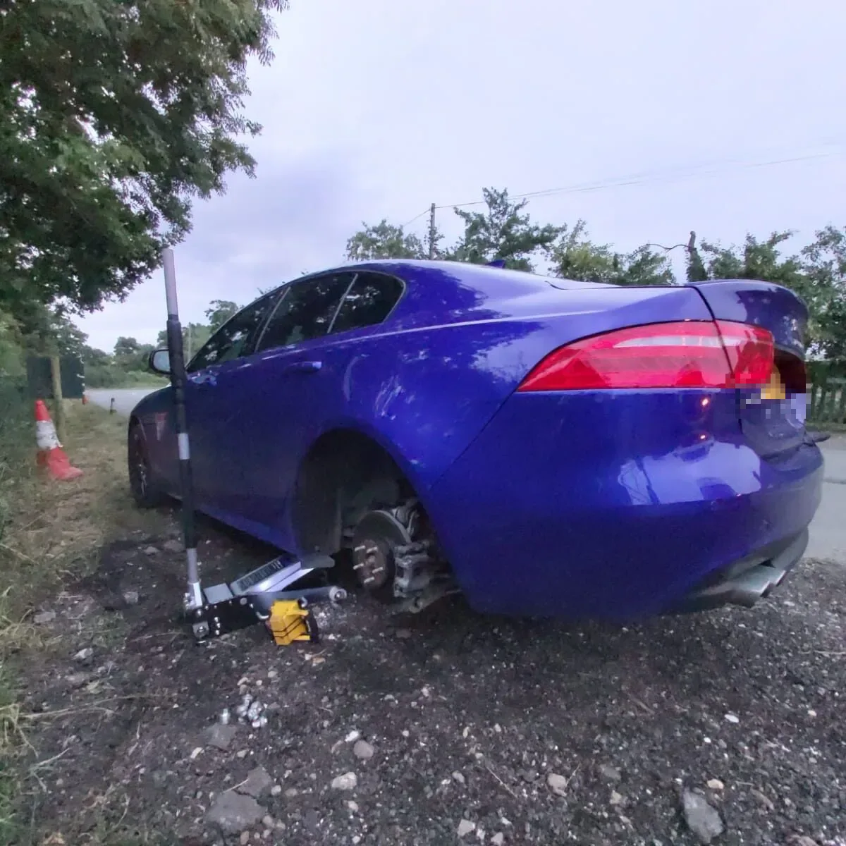 Blue Jaguar XE raised on a trolley jack and axle stand for a wheel change on a rural roadside