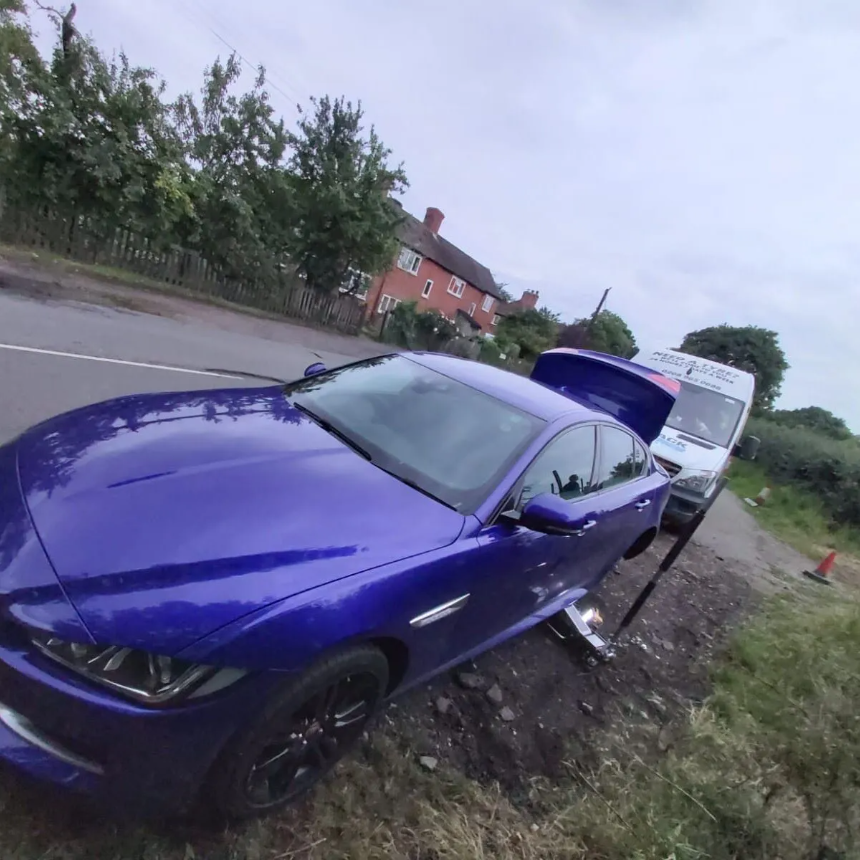 Violet Jaguar XE with a wheel removed on a grass verge during a mobile tyre call-out