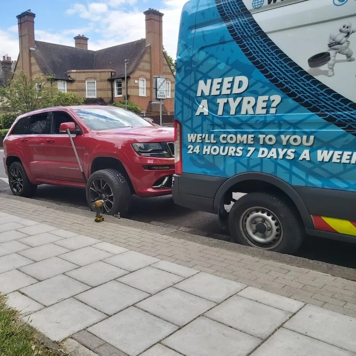 Red Jeep Grand Cherokee SRT with its wheel removed beside the Fastrack Tyres van on a suburban street