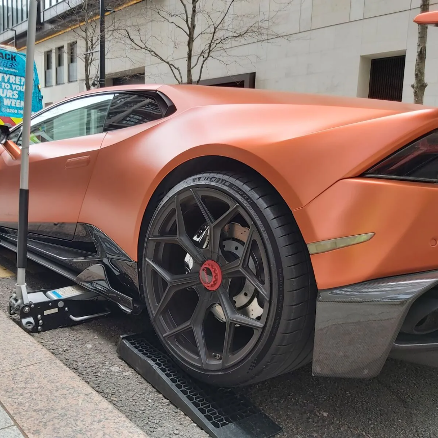 Matte copper Lamborghini Huracan raised on a trolley jack for a wheel change, the Fastrack van behind