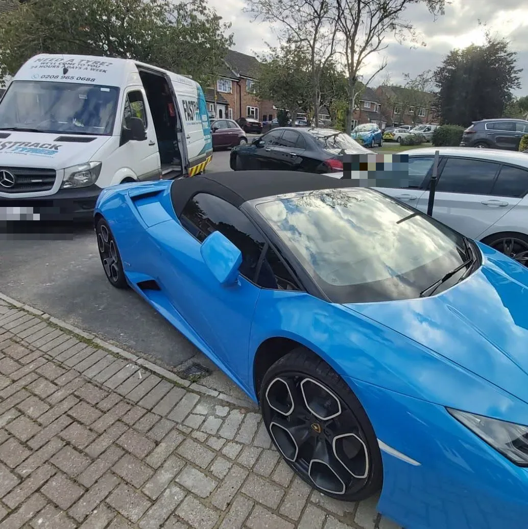 Bright blue Lamborghini Huracan Spyder beside the Fastrack Tyres van during a wheel change on a residential street