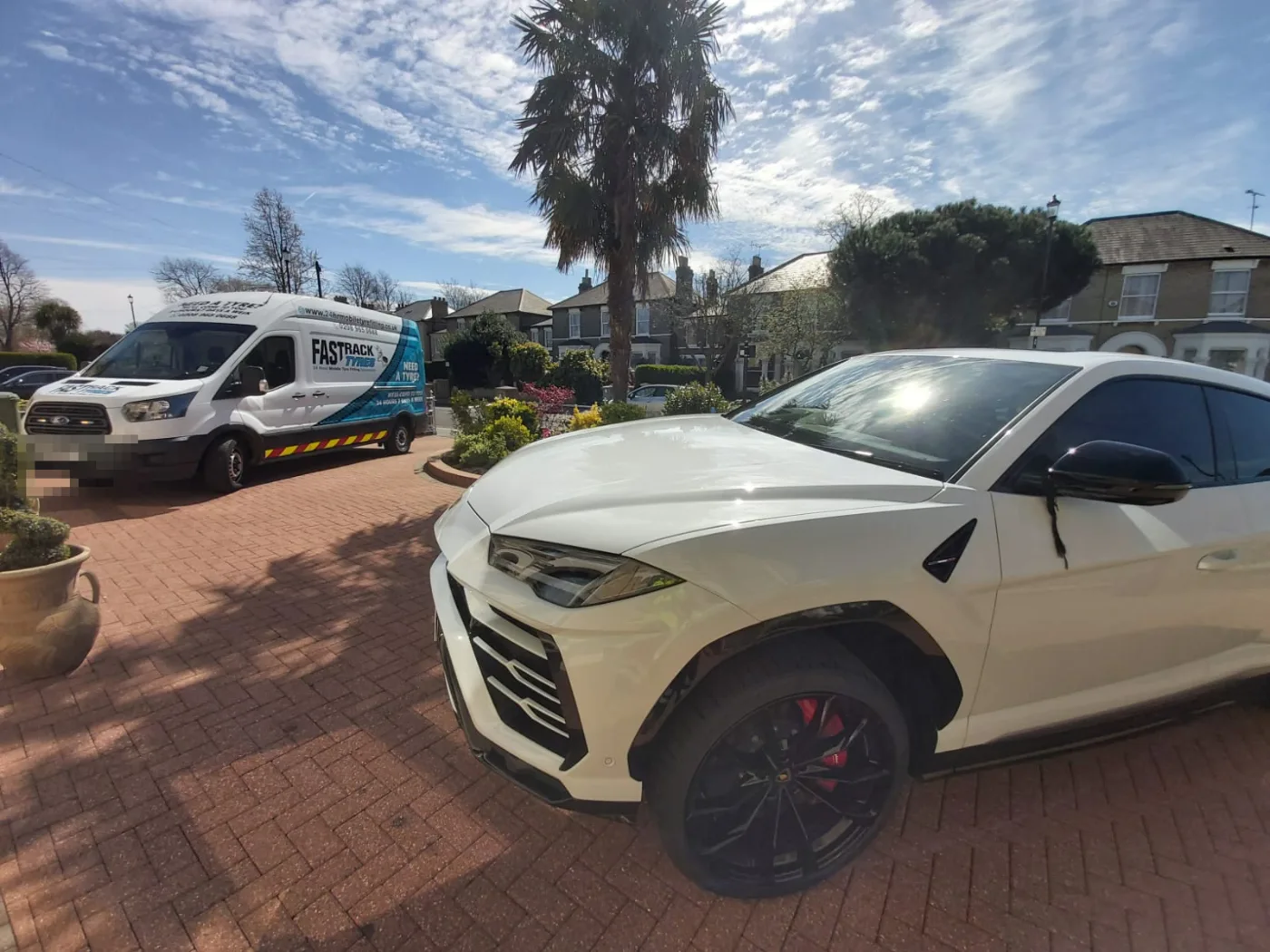 White Lamborghini Urus super-SUV on a London driveway having a tyre changed, Fastrack van in attendance
