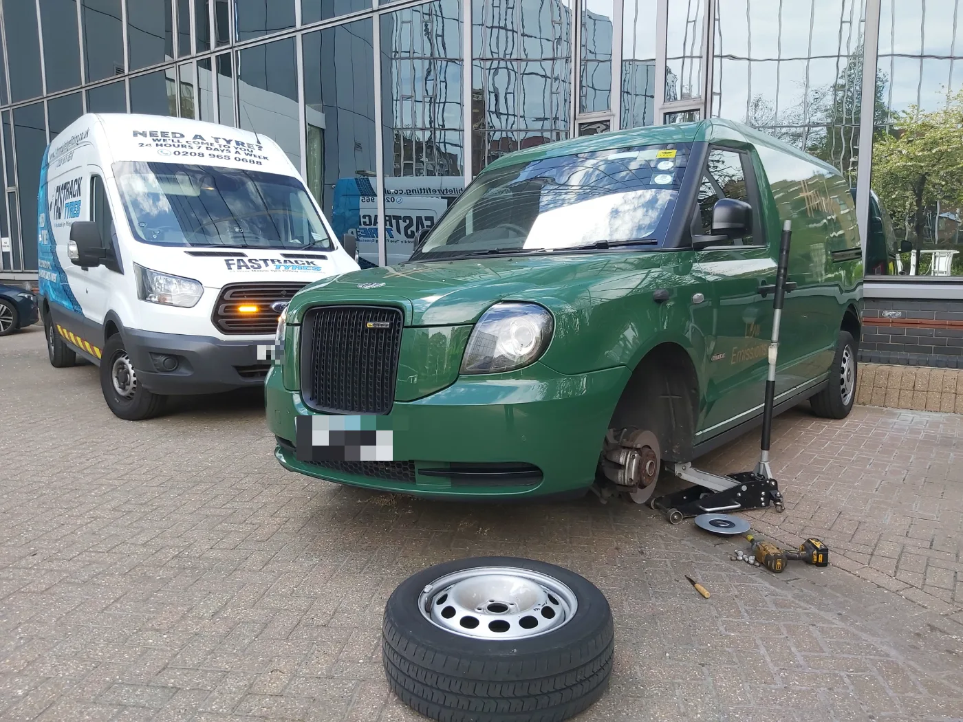 Green LEVC TX electric London taxi up on a jack for a mobile tyre change with a Fastrack van alongside
