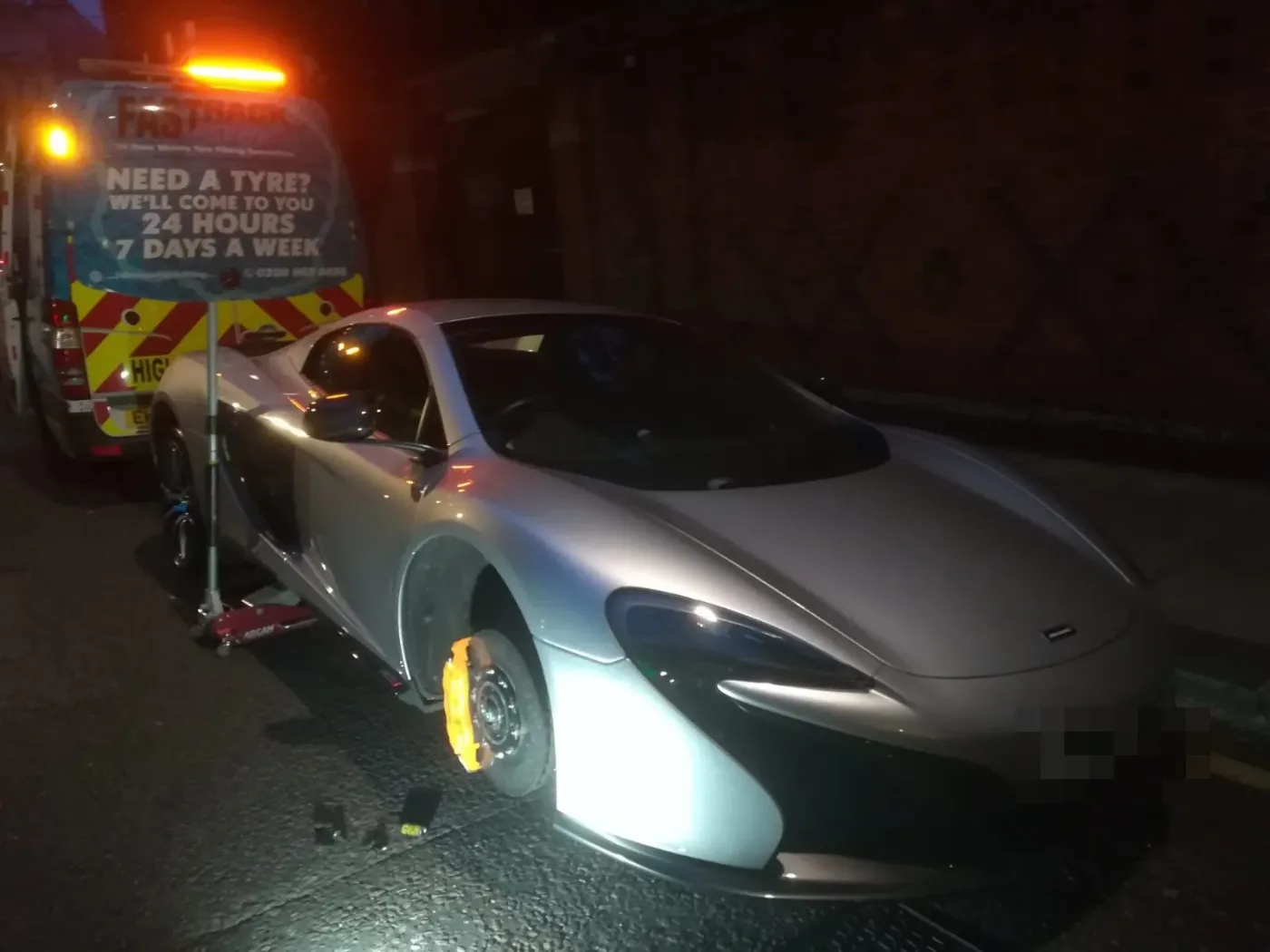 Silver McLaren 650S lit at night beside the Fastrack Tyres van during a wheel change