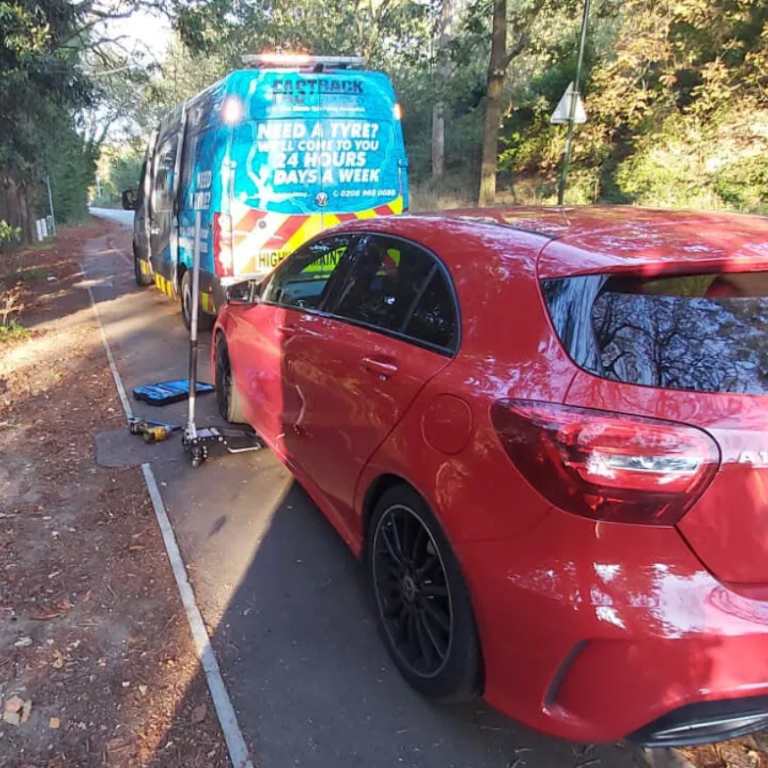 Red Mercedes A-Class on a leafy roadside with the wheel being worked on beside the Fastrack Tyres van