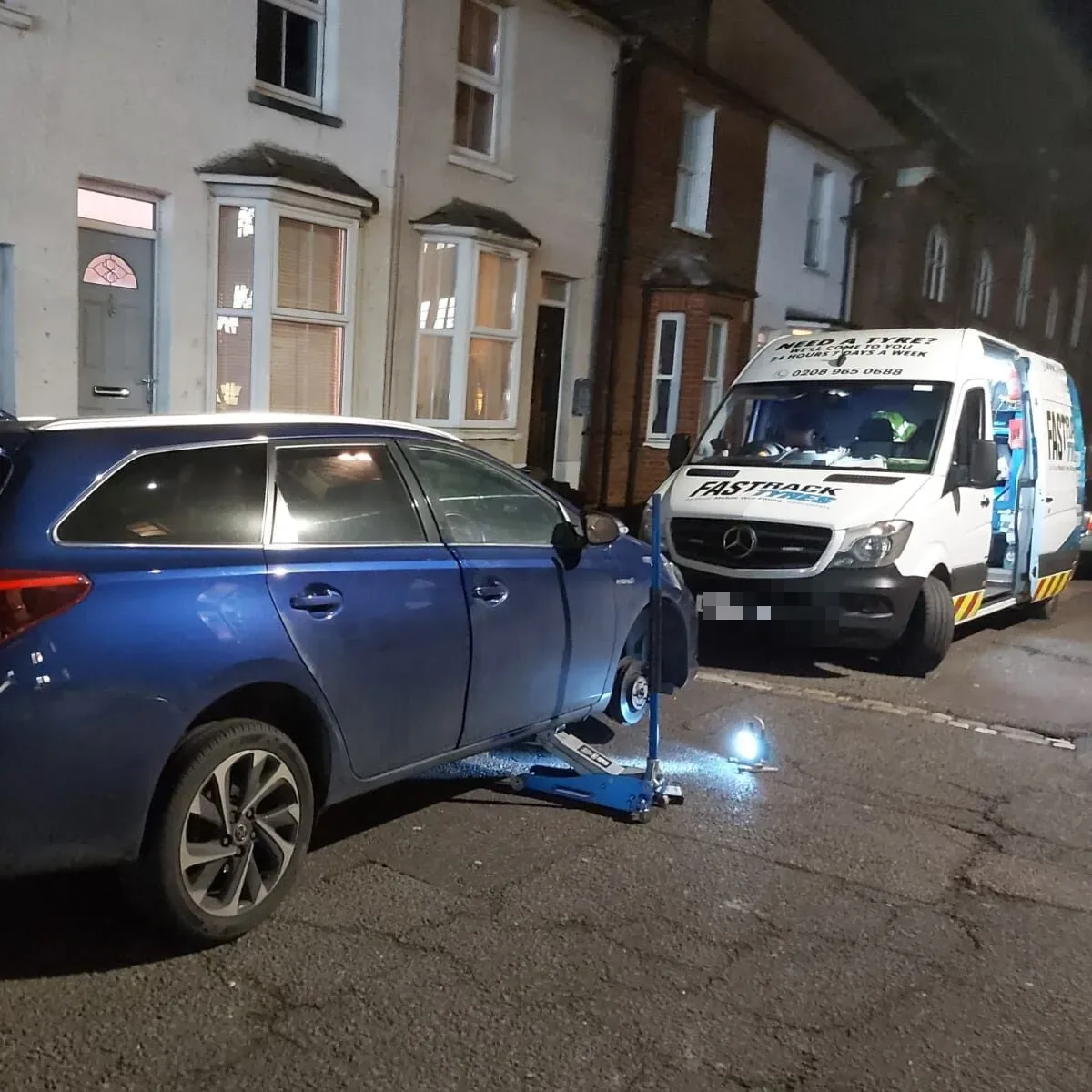 Blue Mitsubishi Outlander PHEV raised on a trolley jack at night with the Fastrack Tyres van behind
