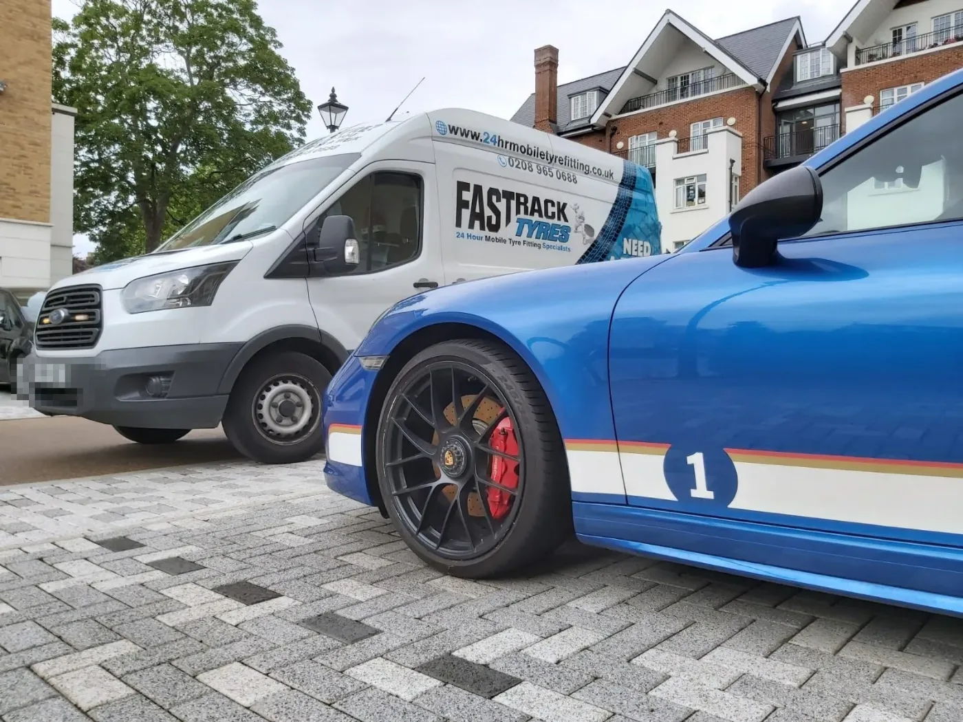 Blue Porsche 911 in number-1 race livery with the Fastrack Tyres van behind during a wheel change