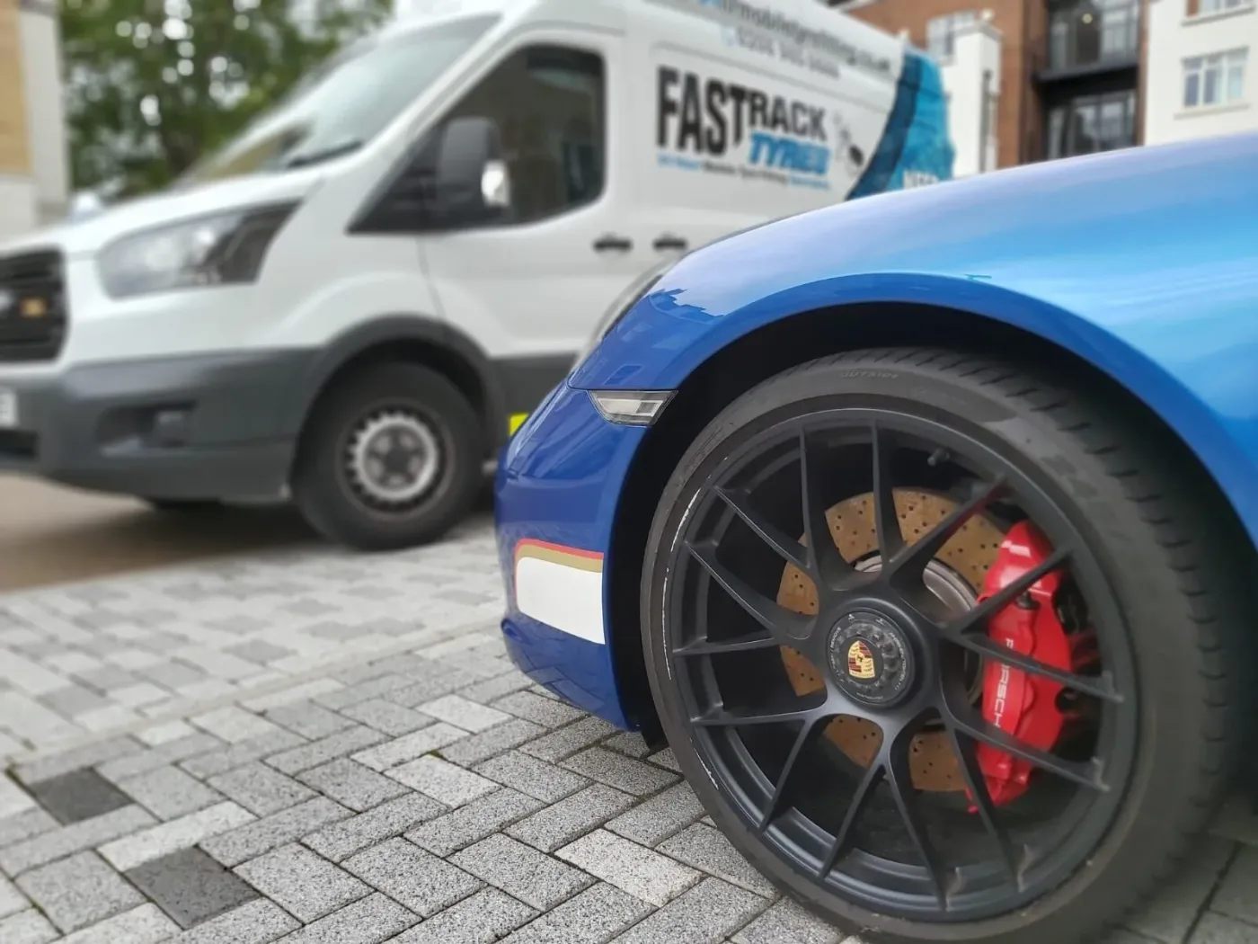 Blue Porsche 911 GTS wheel with red caliper and ceramic disc beside the Fastrack Tyres van on block paving