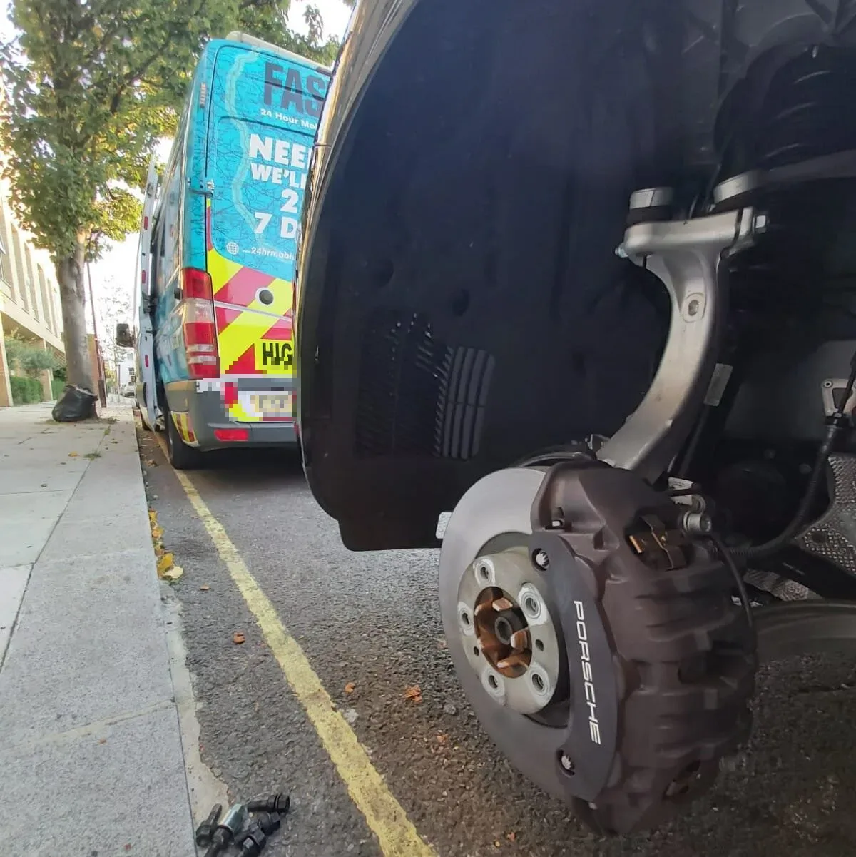 Close-up of a Porsche brake caliper and hub with the wheel removed and the Fastrack Tyres van behind