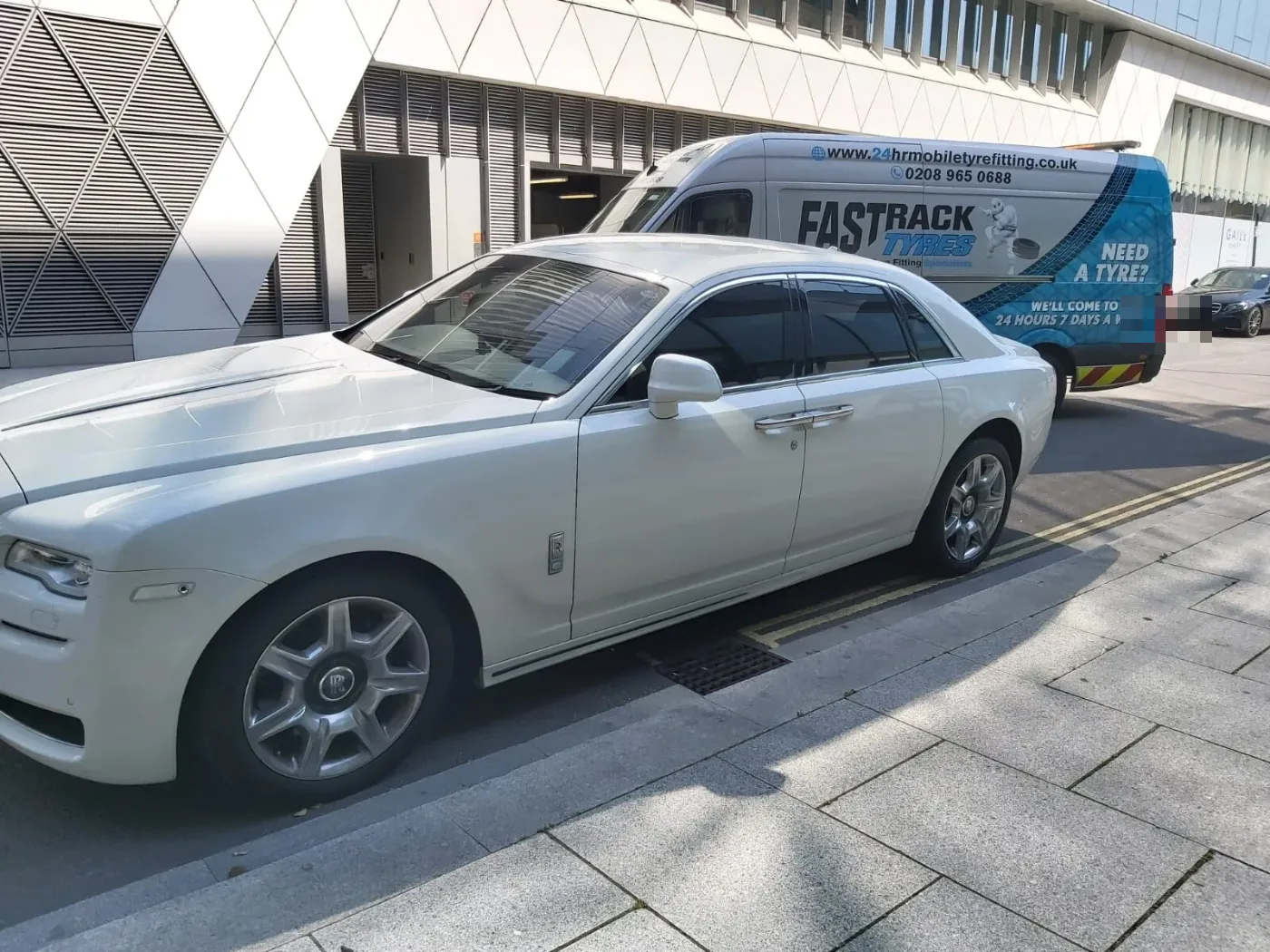 White Rolls-Royce Ghost parked kerbside by a modern building with the Fastrack Tyres van behind