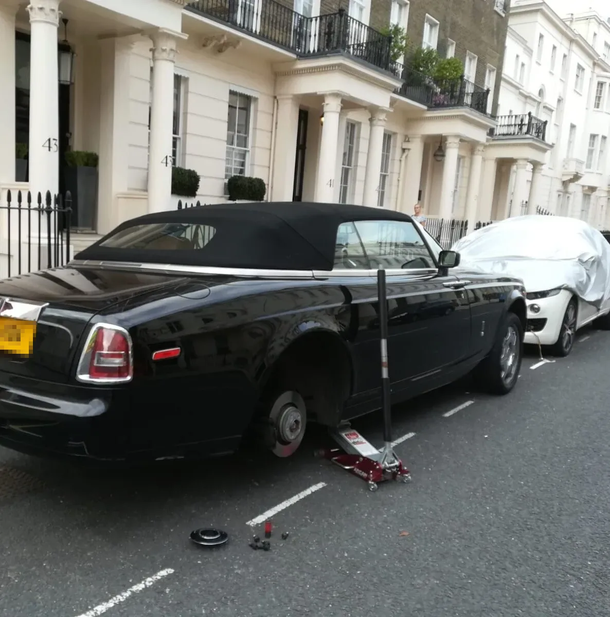 Black Rolls-Royce Phantom Drophead Coupe raised on a trolley jack for a wheel change outside Belgravia townhouses