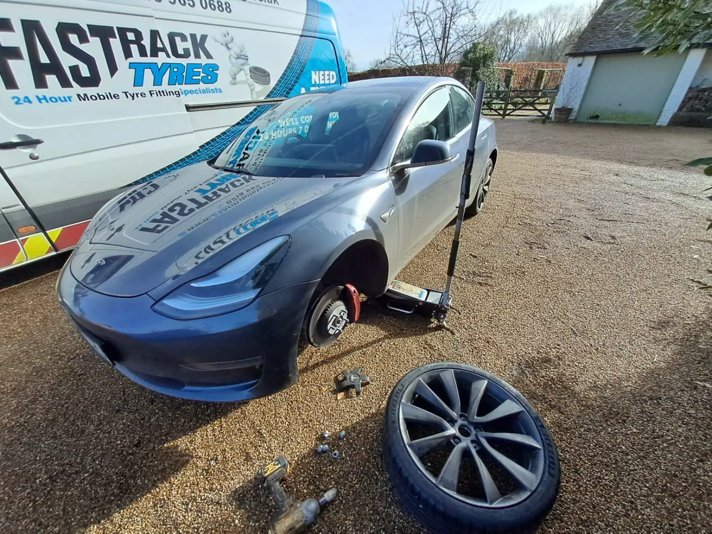 Grey Tesla Model 3 having a wheel changed on a gravel driveway